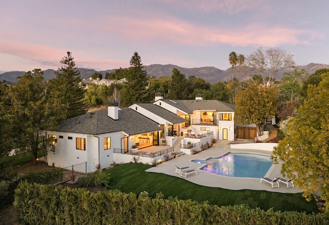 back of house at dusk with stucco siding, a lawn, a fenced backyard, a mountain view, and a chimney