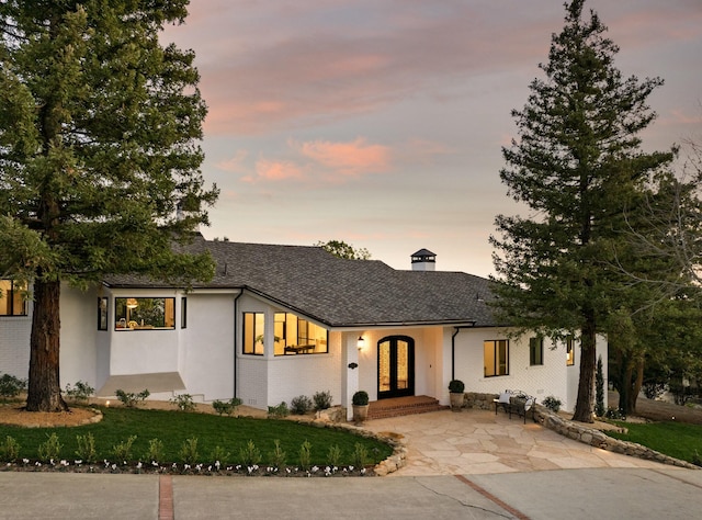 view of front of property featuring french doors, brick siding, and a chimney