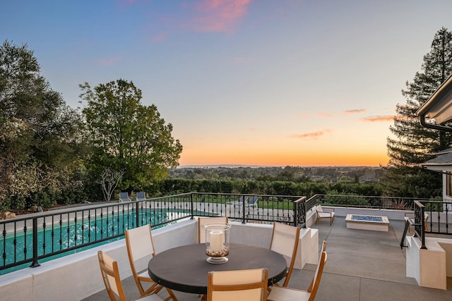 patio terrace at dusk featuring a fenced in pool and an outdoor fire pit