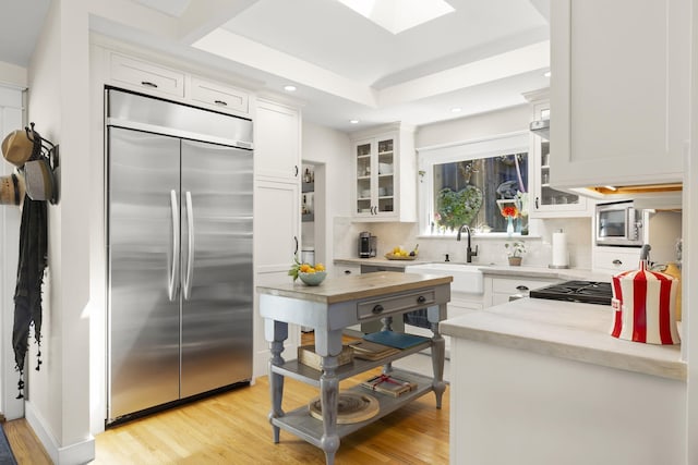 kitchen with a skylight, white cabinetry, sink, light stone counters, and stainless steel appliances