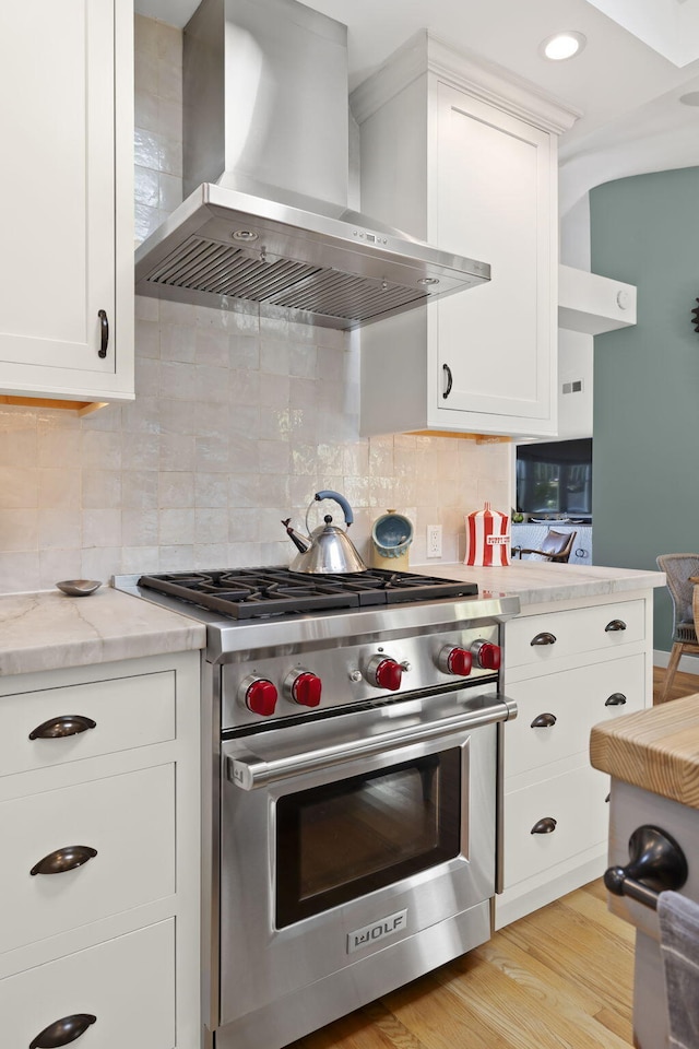 kitchen featuring white cabinetry, decorative backsplash, light hardwood / wood-style floors, luxury stove, and wall chimney exhaust hood