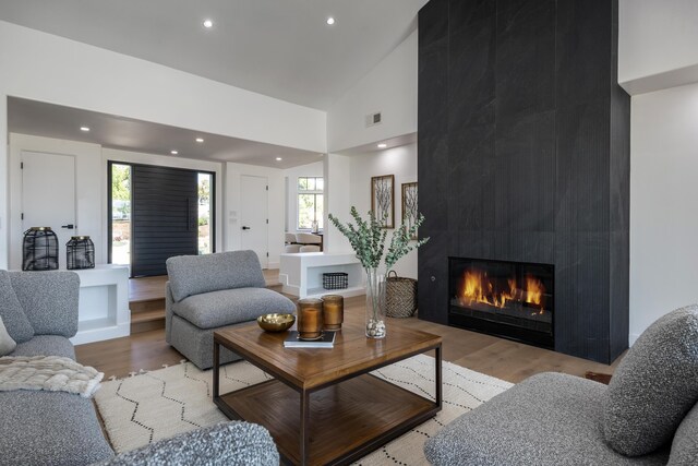 living room featuring a fireplace, high vaulted ceiling, and light wood-type flooring