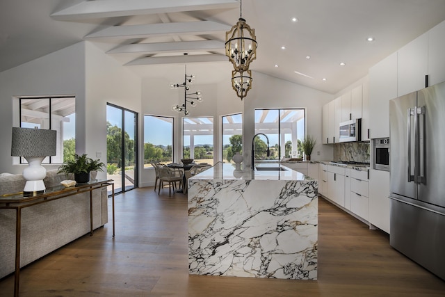 kitchen with appliances with stainless steel finishes, white cabinetry, sink, backsplash, and a center island with sink