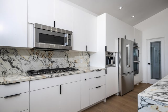 kitchen featuring dark wood-type flooring, stainless steel appliances, tasteful backsplash, light stone countertops, and white cabinets