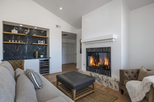 living room with hardwood / wood-style floors, high vaulted ceiling, wine cooler, bar, and a high end fireplace