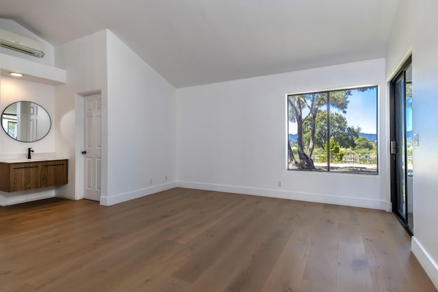 unfurnished bedroom with wood-type flooring, vaulted ceiling, sink, and a wall mounted AC