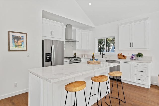 kitchen featuring a breakfast bar, stainless steel appliances, lofted ceiling, white cabinets, and wall chimney exhaust hood