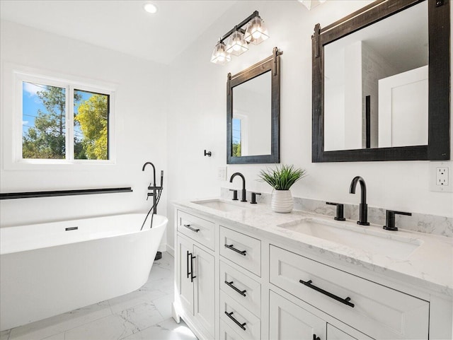 bathroom with double vanity, marble finish floor, a freestanding bath, and a sink