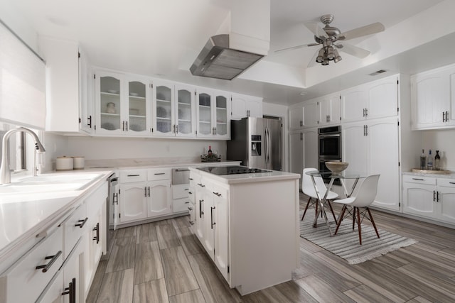 kitchen featuring wall chimney range hood, a kitchen island, white cabinets, and appliances with stainless steel finishes