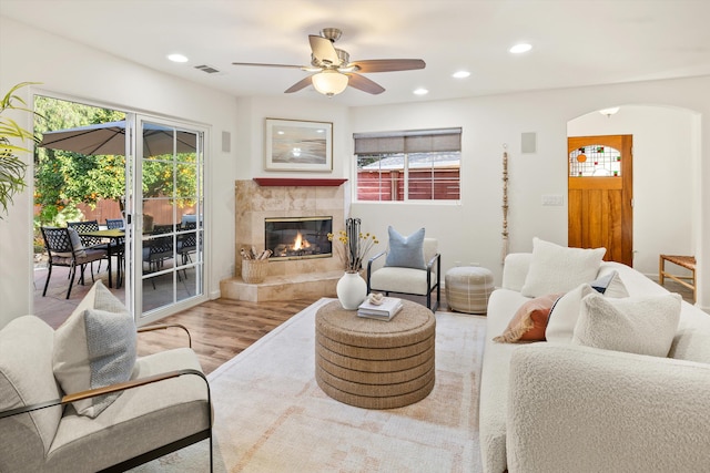 living room featuring ceiling fan, plenty of natural light, a fireplace, and light hardwood / wood-style flooring