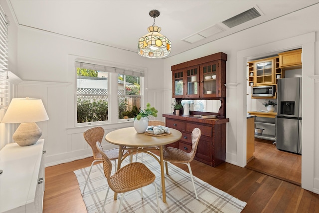 dining room with dark wood-type flooring, a wainscoted wall, visible vents, and a decorative wall