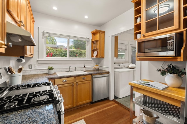 kitchen with open shelves, stainless steel appliances, washing machine and dryer, a sink, and wood finished floors