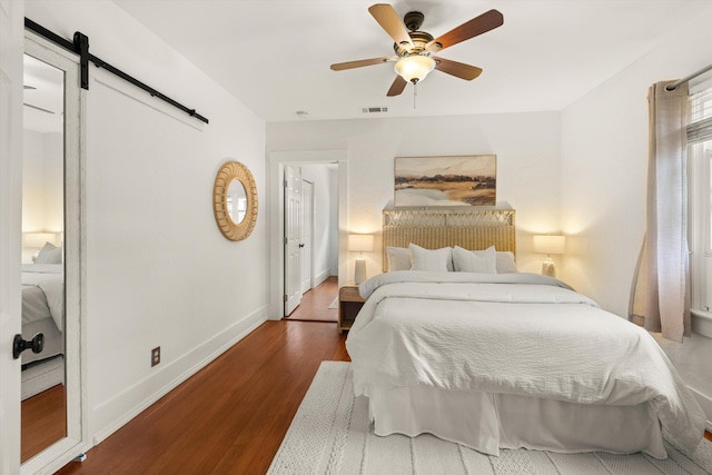 bedroom featuring ceiling fan, a barn door, and dark hardwood / wood-style flooring