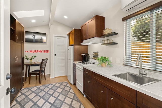 kitchen featuring white appliances, vaulted ceiling with skylight, a wall mounted air conditioner, under cabinet range hood, and a sink