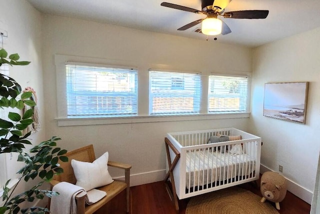 bedroom with a crib, wood finished floors, a ceiling fan, and baseboards