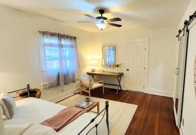 bedroom featuring a barn door, dark wood-type flooring, a ceiling fan, and baseboards