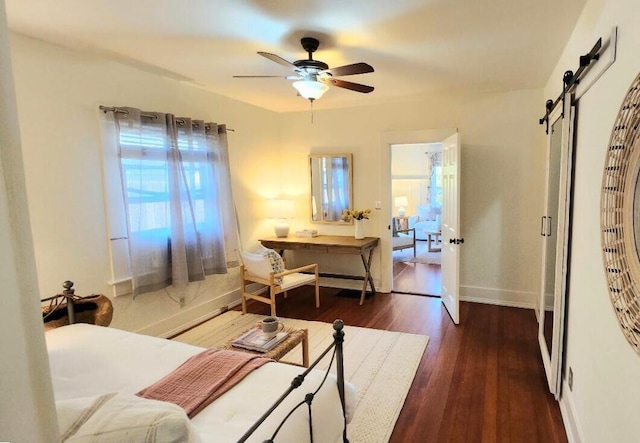 bedroom with dark wood-style floors, a barn door, baseboards, and ceiling fan