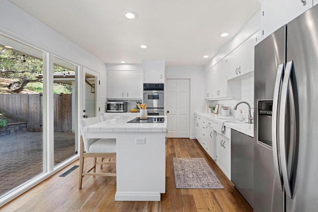 kitchen featuring appliances with stainless steel finishes, white cabinetry, a center island, light hardwood / wood-style floors, and tile countertops