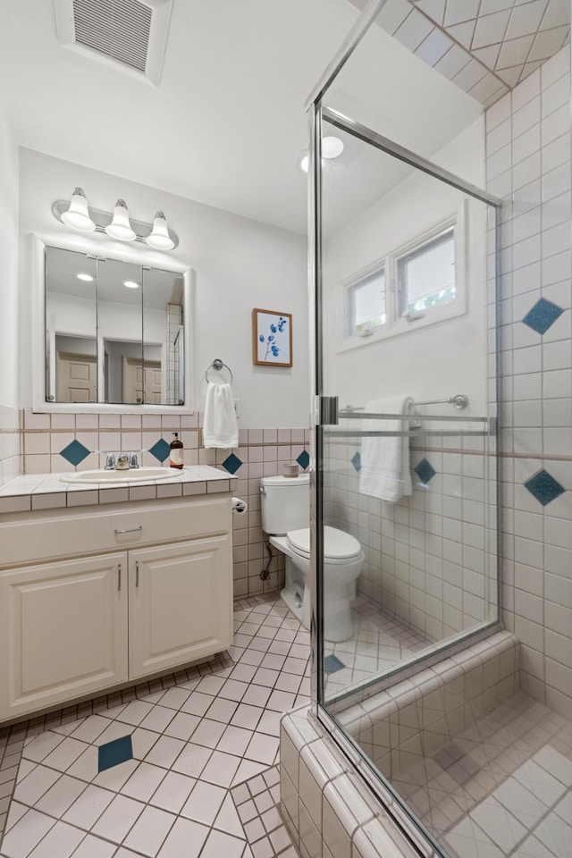 bathroom with toilet, tile walls, vanity, a shower with door, and tile patterned flooring