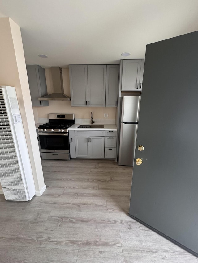 kitchen with appliances with stainless steel finishes, sink, gray cabinetry, light wood-type flooring, and wall chimney exhaust hood