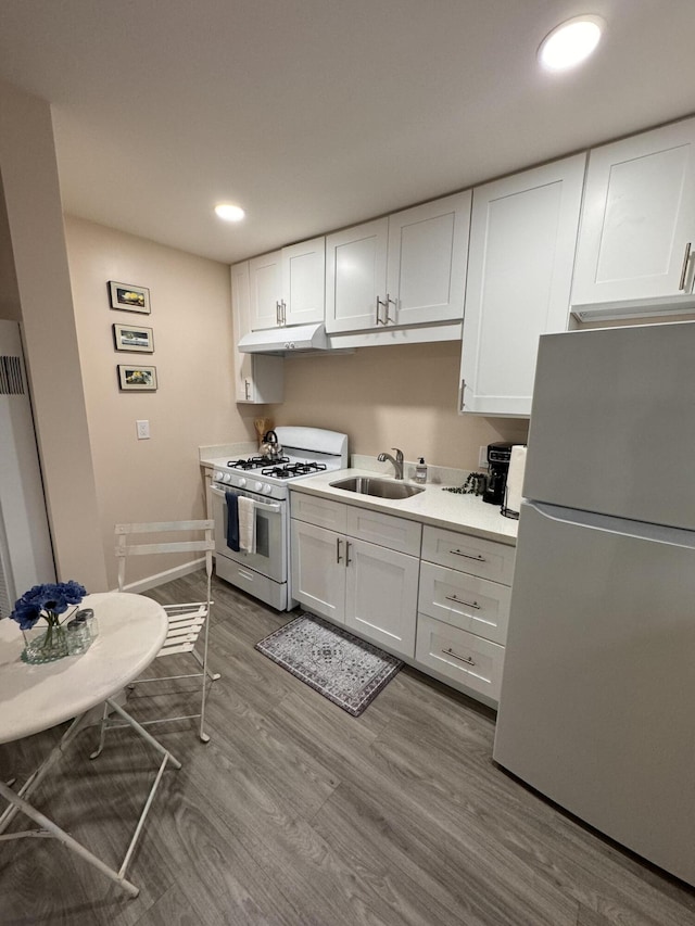 kitchen with sink, white appliances, hardwood / wood-style floors, and white cabinets