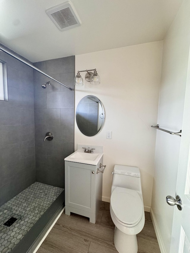 bathroom featuring vanity, hardwood / wood-style floors, toilet, and tiled shower