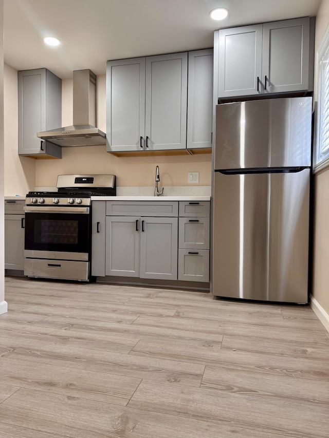 kitchen with wall chimney exhaust hood, sink, appliances with stainless steel finishes, gray cabinets, and light hardwood / wood-style floors