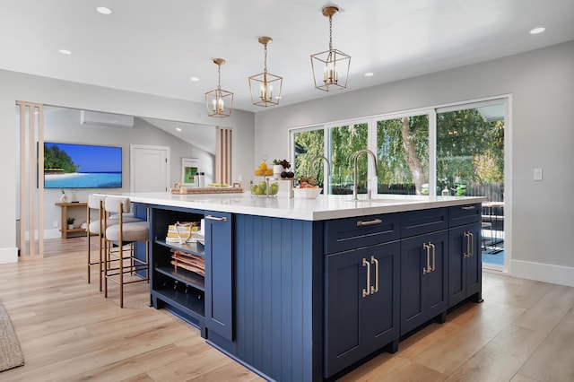 kitchen featuring pendant lighting, sink, light hardwood / wood-style flooring, blue cabinets, and a large island with sink