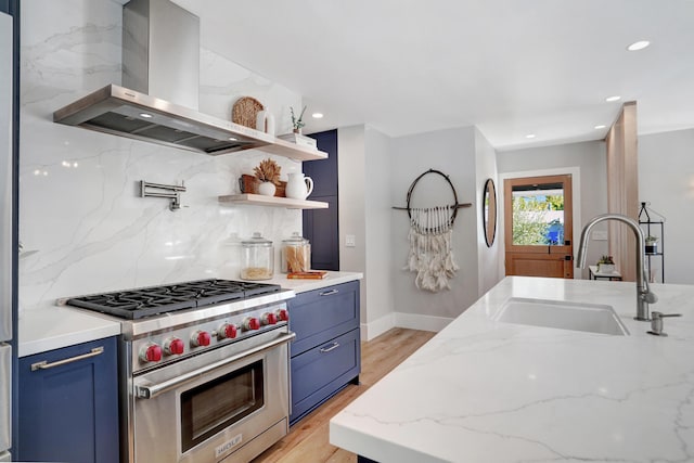 kitchen with blue cabinetry, sink, luxury stove, light stone countertops, and wall chimney range hood