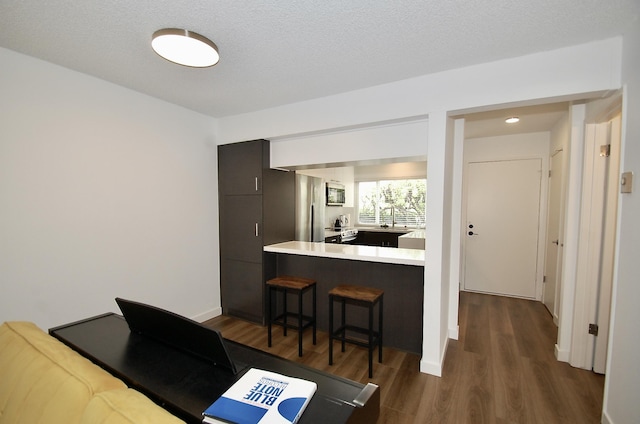 kitchen with dark wood-type flooring, a kitchen breakfast bar, kitchen peninsula, and a textured ceiling