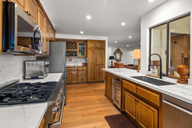 kitchen with sink, appliances with stainless steel finishes, light stone counters, light hardwood / wood-style floors, and beverage cooler