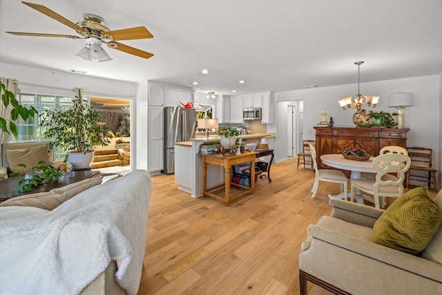 living room featuring ceiling fan with notable chandelier and light hardwood / wood-style flooring