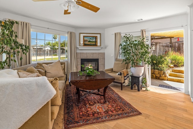 living room with ceiling fan, a tiled fireplace, and hardwood / wood-style floors