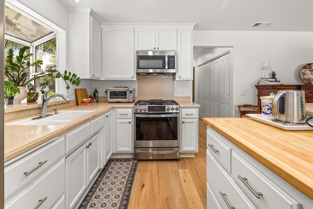 kitchen with appliances with stainless steel finishes, sink, white cabinets, and light hardwood / wood-style flooring