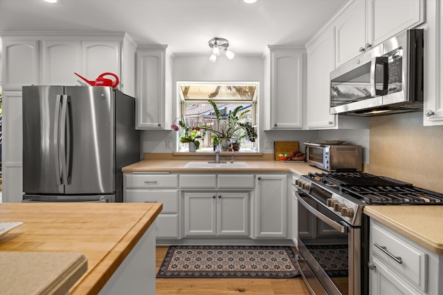 kitchen with appliances with stainless steel finishes, white cabinetry, sink, butcher block counters, and light hardwood / wood-style flooring