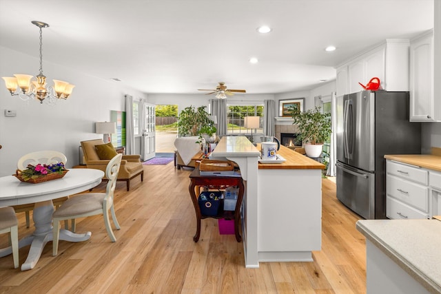 kitchen with a tile fireplace, stainless steel refrigerator, white cabinets, hanging light fixtures, and light hardwood / wood-style flooring