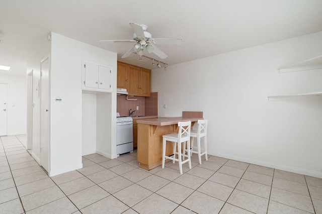 kitchen with light tile patterned flooring, kitchen peninsula, tasteful backsplash, a kitchen breakfast bar, and white stove