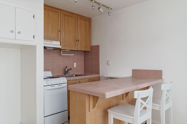 kitchen with tile countertops, white range with electric stovetop, sink, a breakfast bar area, and decorative backsplash