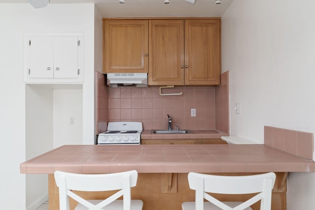 kitchen featuring a kitchen bar, tile countertops, sink, and stove