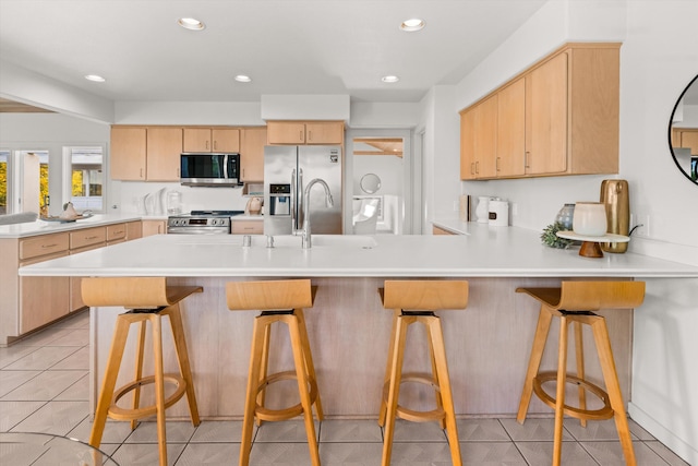 kitchen with a breakfast bar, light brown cabinetry, light tile patterned floors, appliances with stainless steel finishes, and kitchen peninsula