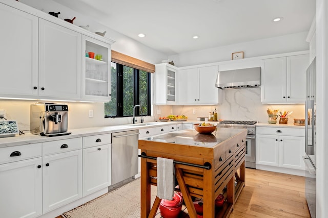 kitchen featuring high quality appliances, wall chimney exhaust hood, light wood-type flooring, sink, and white cabinetry