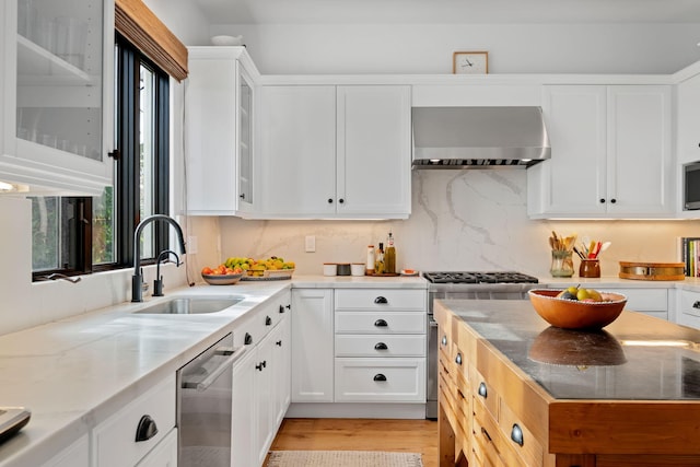 kitchen with sink, light stone counters, white cabinetry, wall chimney range hood, and stainless steel appliances