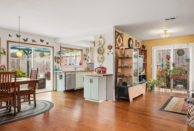 kitchen featuring sink, light wood-type flooring, stainless steel dishwasher, kitchen peninsula, and pendant lighting