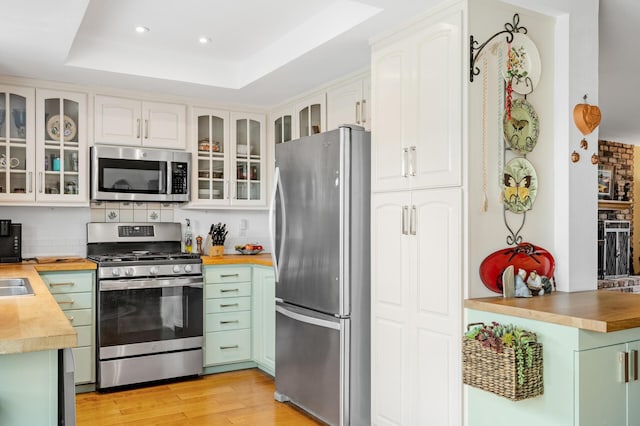 kitchen featuring appliances with stainless steel finishes, butcher block counters, white cabinets, a raised ceiling, and light wood-type flooring