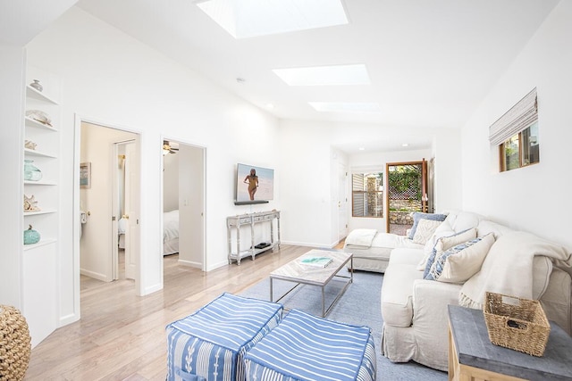 living room with lofted ceiling with skylight, light hardwood / wood-style floors, and built in shelves