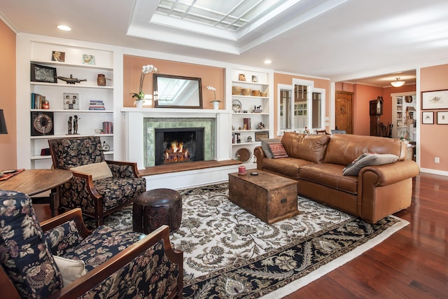 living room with crown molding, built in features, a tile fireplace, dark hardwood / wood-style floors, and a tray ceiling