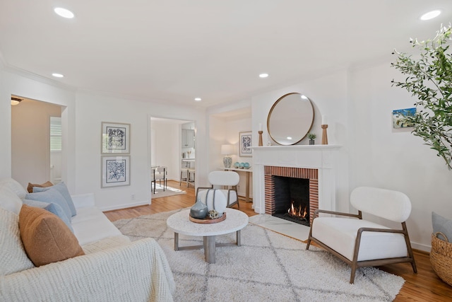 living room with crown molding, a brick fireplace, and light wood-type flooring