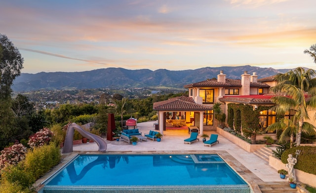 pool at dusk featuring a mountain view, an outdoor living space, and a water slide