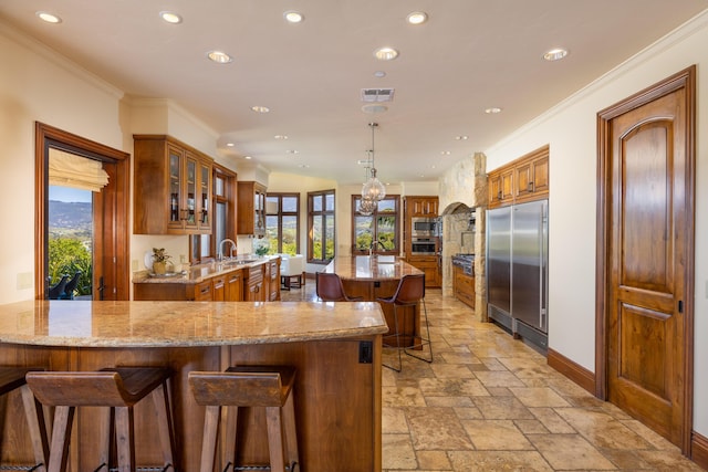 kitchen featuring sink, a breakfast bar area, built in appliances, kitchen peninsula, and light stone countertops