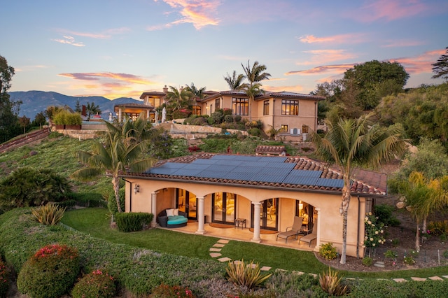 back house at dusk with a mountain view, a patio area, and solar panels